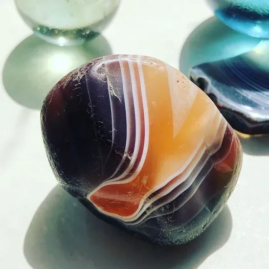 A polished agate with bands of orange, cream and dark blue, beside glass marbles.