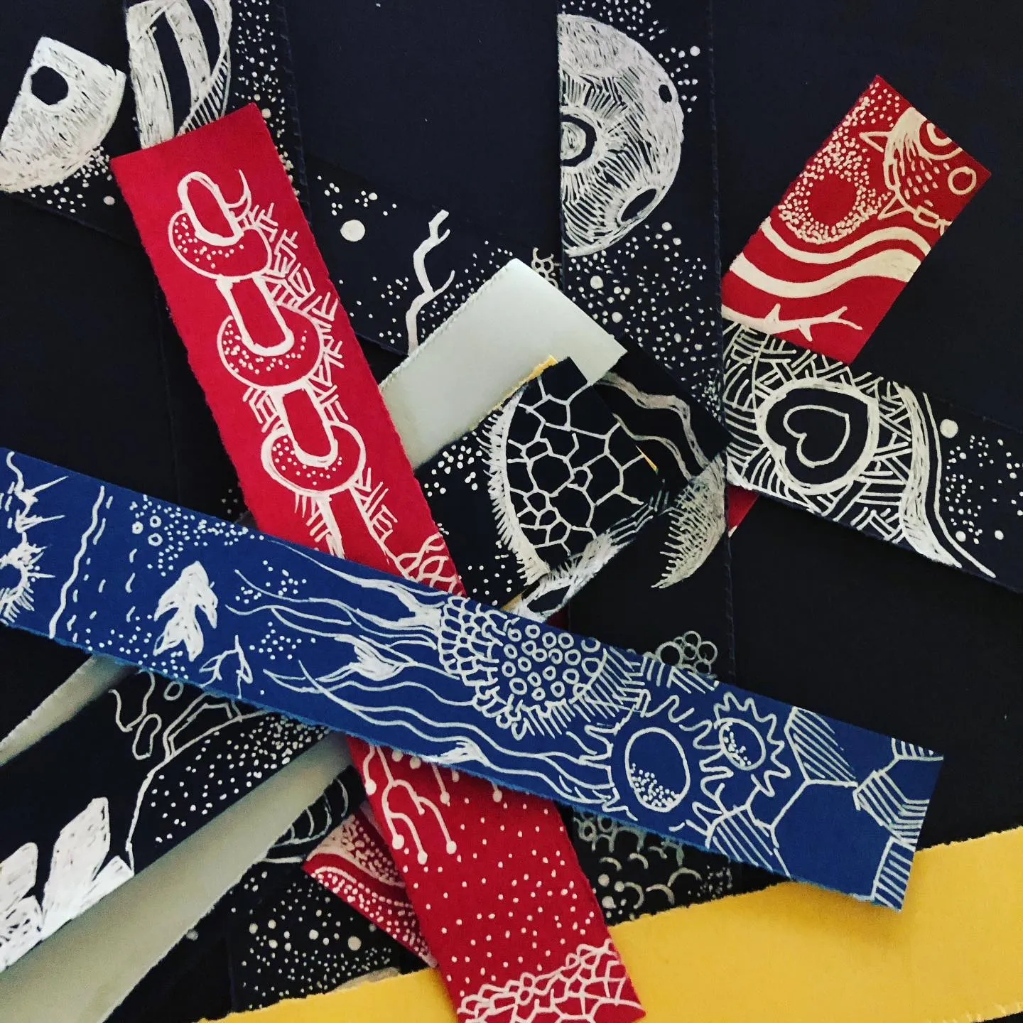 A heap of hand-drawn bookmarks in white ink on dark, red and blue card: moons, a turtle shell, a heart, linked rings, and a blue strip with a fish, jellyfish tendrils and a sun.