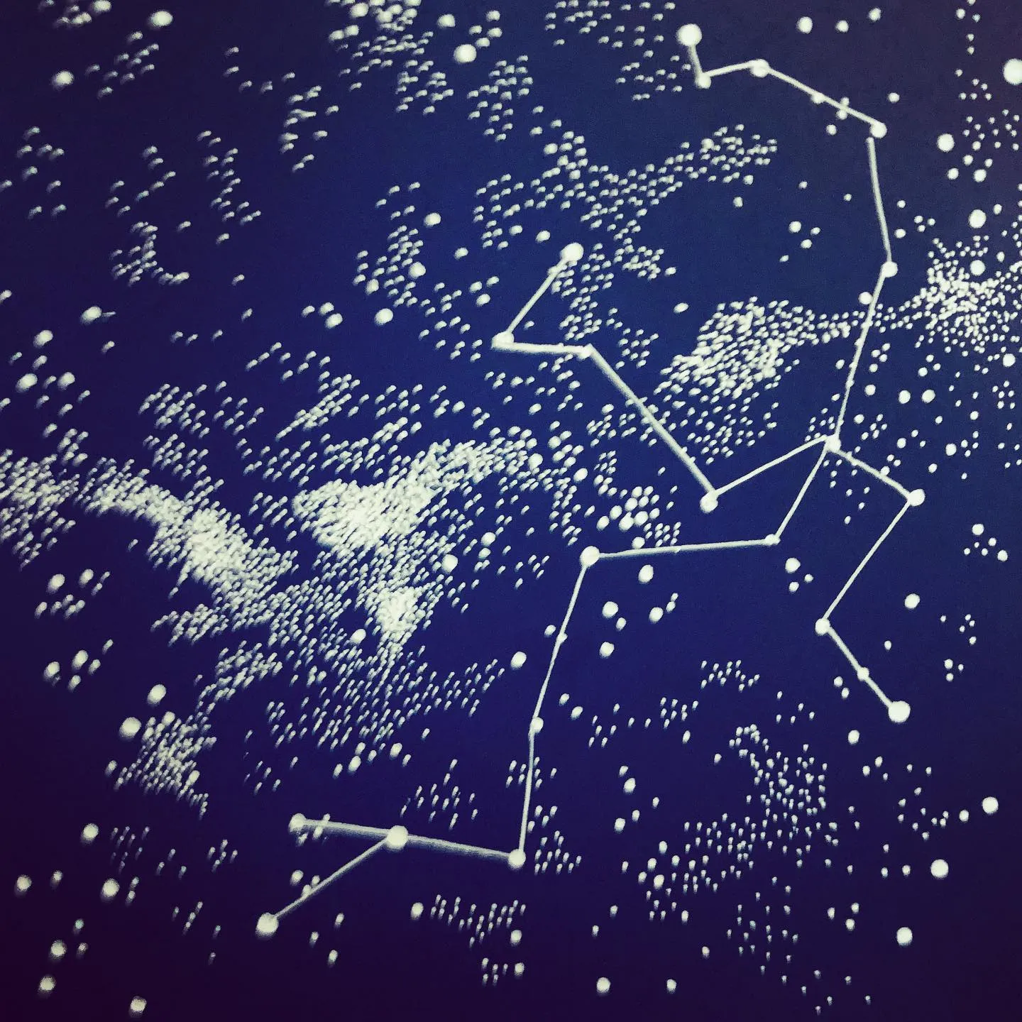 White ink stars and a dotted constellation drawn over a deep blue night sky, with a misty band of stars.