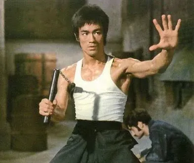 Bruce Lee in a fighting stance, holding nunchaku.
