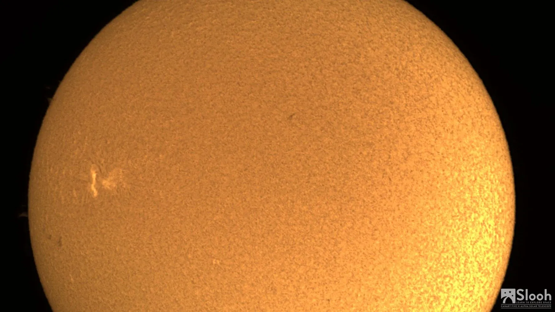 The Sun through a solar filter: a glowing orange disc with a small bright flare near its edge.